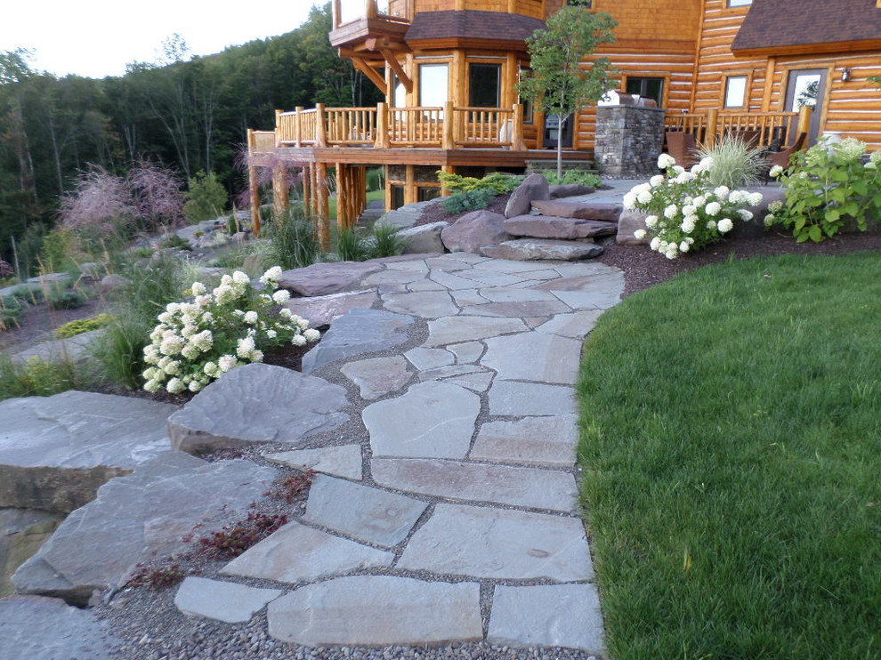 This is an example of a large country sloped full sun xeriscape in New York with a garden path and natural stone pavers.