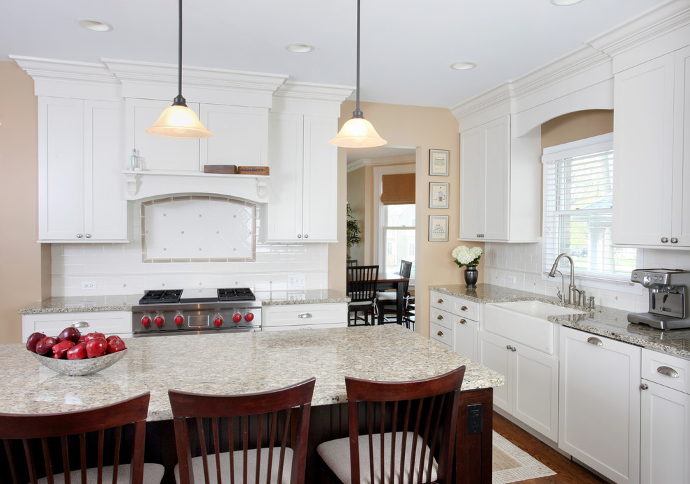 This is an example of a large traditional l-shaped eat-in kitchen in Chicago with a farmhouse sink, shaker cabinets, white cabinets, granite benchtops, white splashback, subway tile splashback, stainless steel appliances, medium hardwood floors and with island.