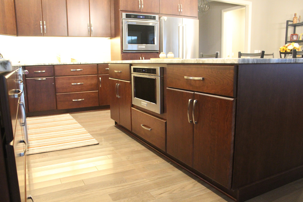 This is an example of a large modern l-shaped eat-in kitchen in Detroit with dark wood cabinets, stainless steel appliances, with island, an undermount sink, flat-panel cabinets, quartzite benchtops, grey splashback, glass tile splashback, medium hardwood floors, brown floor and grey benchtop.