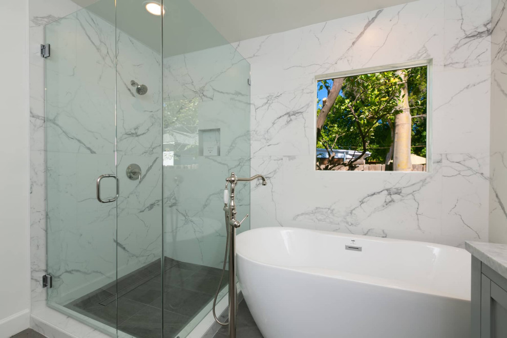 Large contemporary master bathroom in Los Angeles with recessed-panel cabinets, grey cabinets, a freestanding tub, a corner shower, a one-piece toilet, white tile, marble, white walls, ceramic floors, an undermount sink, marble benchtops, grey floor, a hinged shower door, grey benchtops, a double vanity and a freestanding vanity.
