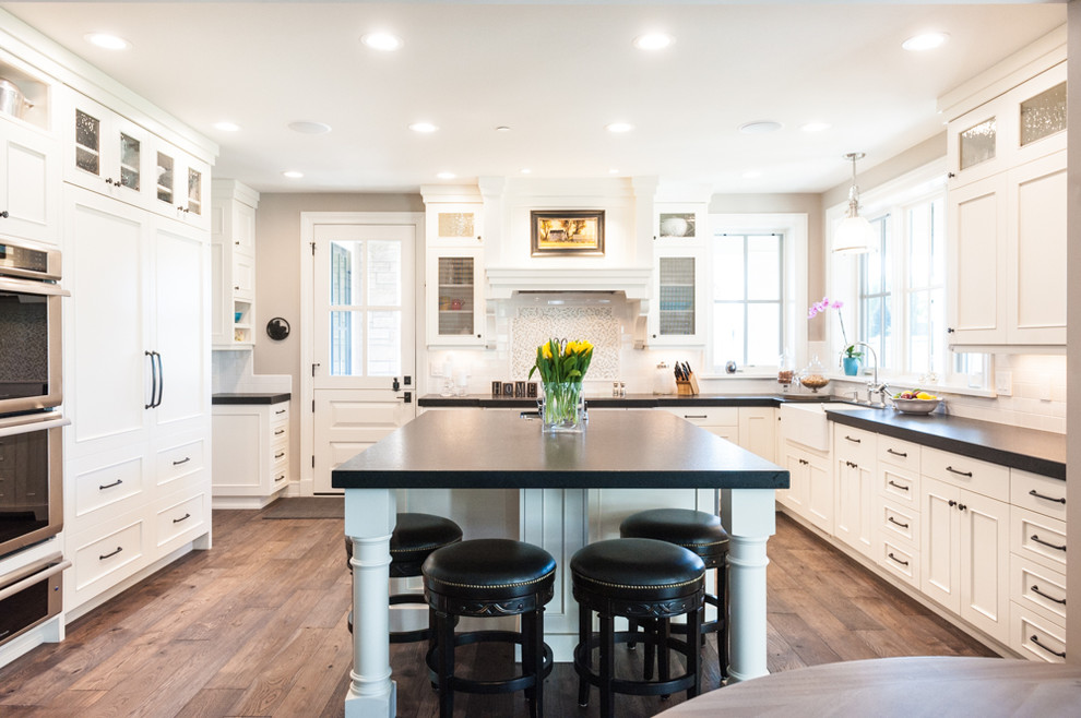 Inspiration for a traditional u-shaped kitchen in Salt Lake City with a farmhouse sink, recessed-panel cabinets, white cabinets, white splashback, dark hardwood floors and with island.