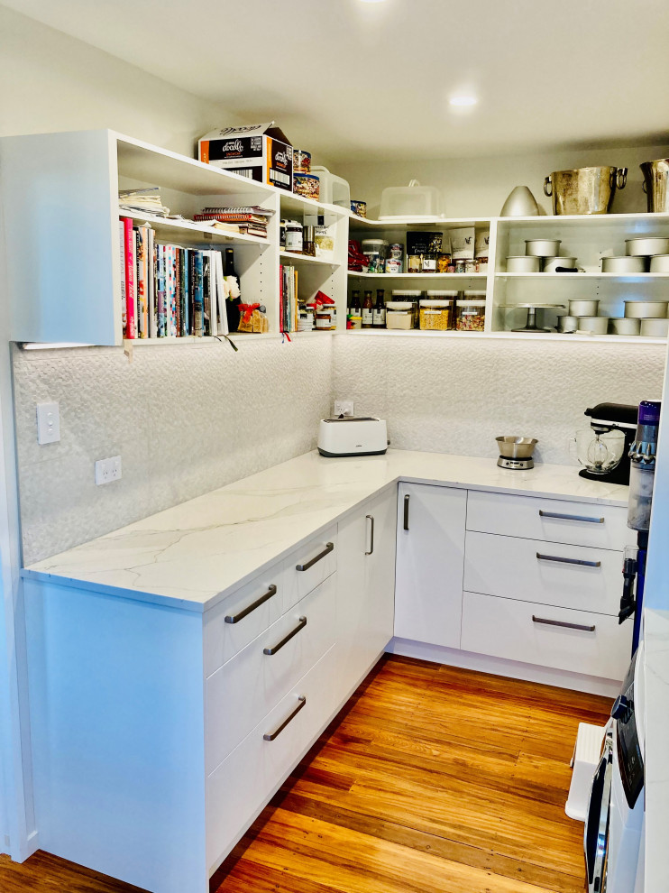 Photo of a small contemporary l-shaped kitchen pantry in Christchurch with white cabinets, quartz benchtops, white splashback, ceramic splashback and white benchtop.