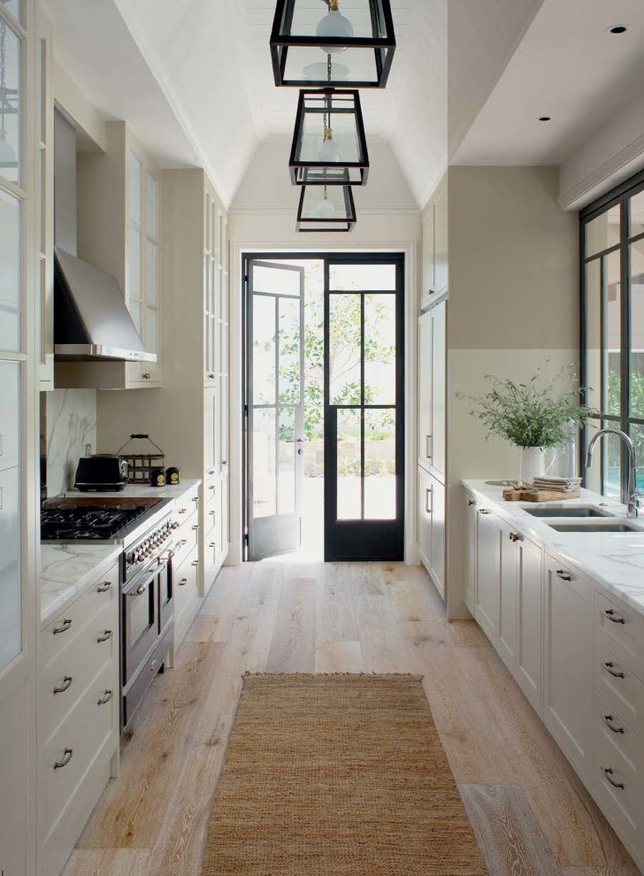 Design ideas for a traditional galley kitchen in Central Coast with a double-bowl sink, shaker cabinets, white cabinets, marble benchtops, white splashback, light hardwood floors and no island.