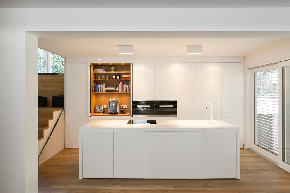 Design ideas for a mid-sized modern galley open plan kitchen in Frankfurt with flat-panel cabinets, white cabinets, medium hardwood floors, with island, panelled appliances and brown floor.