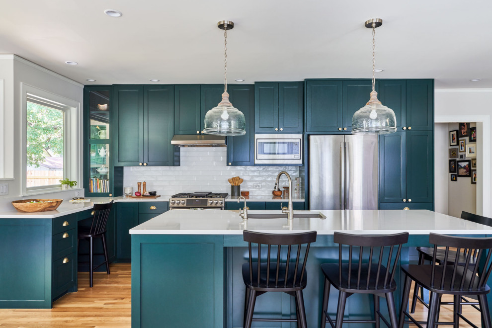 Mid-sized traditional open plan kitchen in Austin with an undermount sink, shaker cabinets, turquoise cabinets, white splashback, stainless steel appliances, medium hardwood floors, with island and white benchtop.