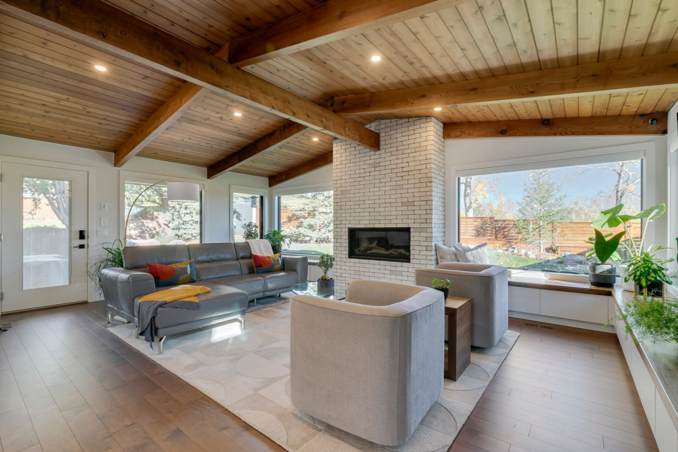 Photo of a midcentury living room with white walls, a brick fireplace surround, brown floors and a vaulted ceiling.