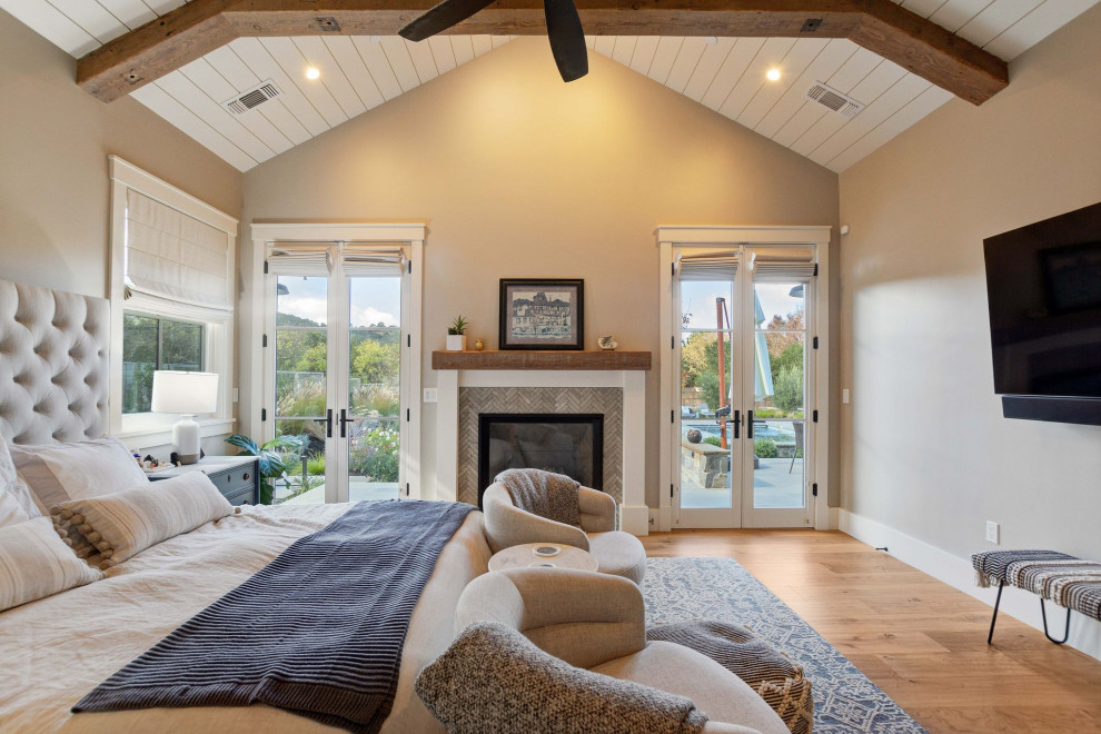 Aménagement d'une grande chambre parentale campagne avec un mur beige, un sol en bois brun, une cheminée standard, un manteau de cheminée en carrelage, un sol marron et un plafond en lambris de bois.