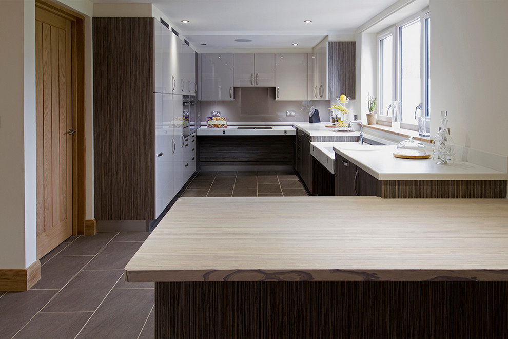 Small contemporary u-shaped open plan kitchen in Buckinghamshire with an integrated sink, flat-panel cabinets, beige cabinets, wood benchtops, beige splashback, glass sheet splashback, stainless steel appliances, porcelain floors, a peninsula and brown floor.
