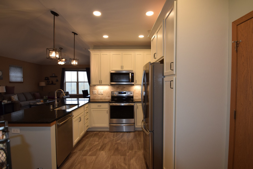 Example of a mid-sized transitional u-shaped vinyl floor kitchen design with a single-bowl sink, shaker cabinets, white cabinets, quartz countertops, multicolored backsplash, stone tile backsplash, stainless steel appliances, a peninsula and black countertops