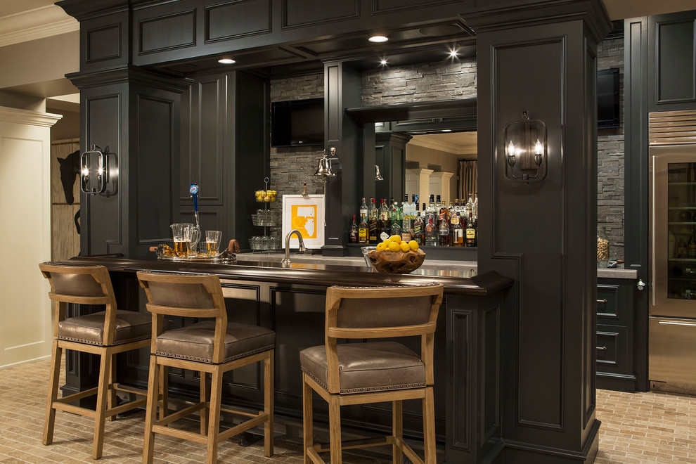 Design ideas for a transitional galley seated home bar in Minneapolis with brick floors, recessed-panel cabinets, black cabinets, wood benchtops, grey splashback, stone tile splashback, beige floor and brown benchtop.
