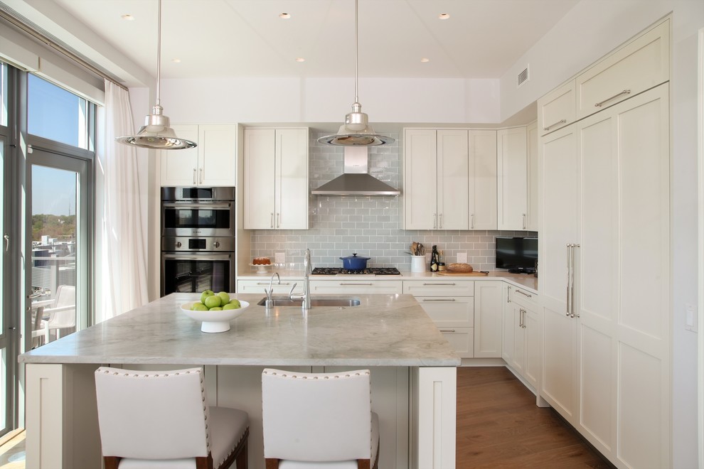 Large transitional l-shaped eat-in kitchen in DC Metro with an undermount sink, shaker cabinets, white cabinets, marble benchtops, grey splashback, subway tile splashback, stainless steel appliances, medium hardwood floors, with island and brown floor.