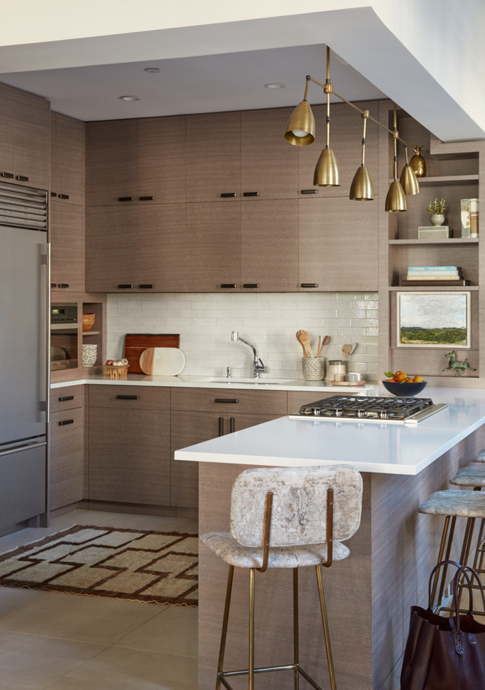 This is an example of a contemporary u-shaped kitchen in New York with an undermount sink, flat-panel cabinets, medium wood cabinets, white splashback, subway tile splashback, stainless steel appliances, a peninsula, quartz benchtops, porcelain floors and brown floor.