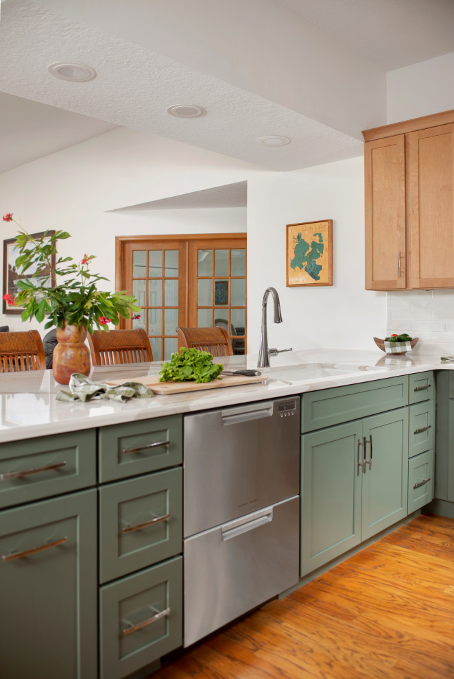 Modern inredning av ett mellanstort beige beige kök, med en enkel diskho, släta luckor, gröna skåp, bänkskiva i kvarts, beige stänkskydd, stänkskydd i keramik, rostfria vitvaror, ljust trägolv, en halv köksö och brunt golv