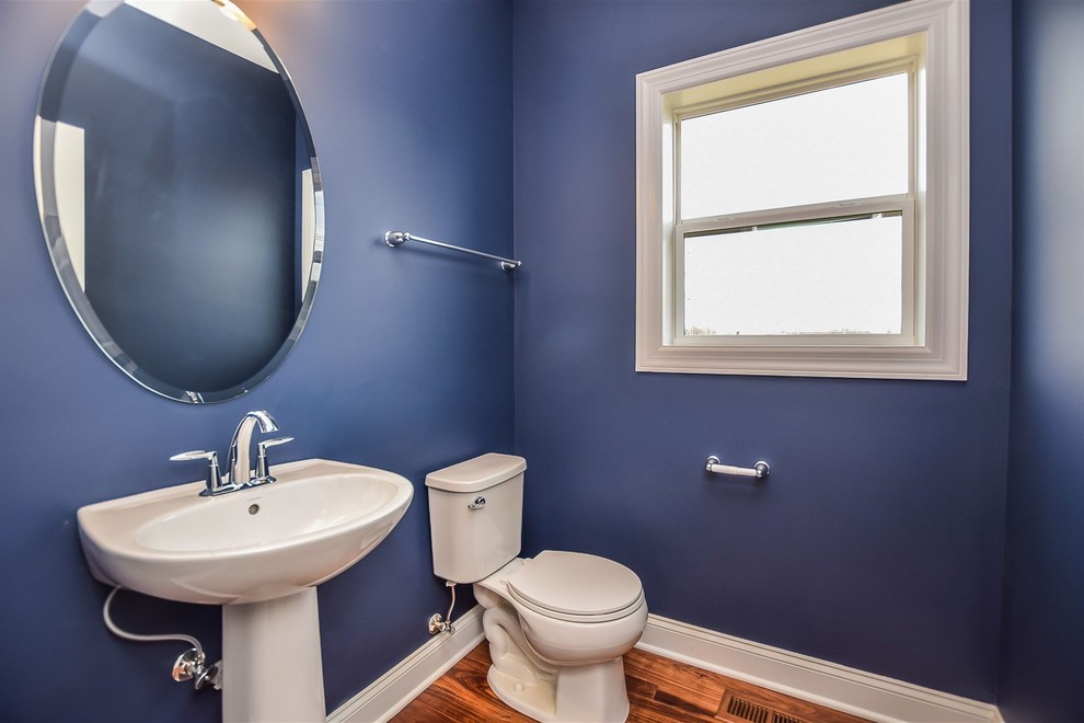 This is an example of a mid-sized traditional powder room in Chicago with a two-piece toilet, blue walls, medium hardwood floors, a pedestal sink and brown floor.