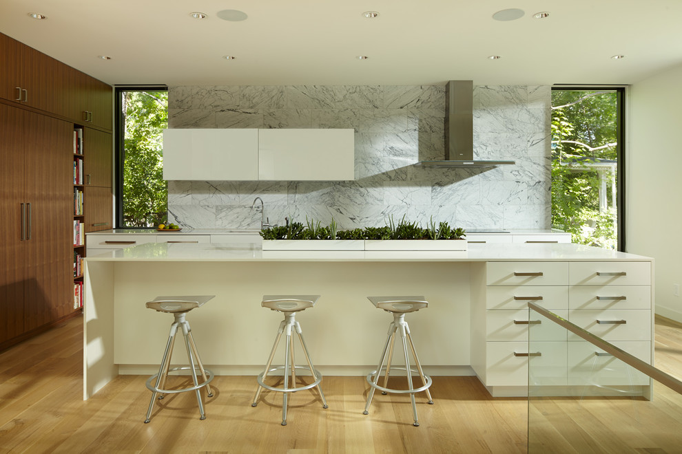 Contemporary u-shaped kitchen in Minneapolis with flat-panel cabinets, white cabinets, white splashback, stainless steel appliances, light hardwood floors and with island.
