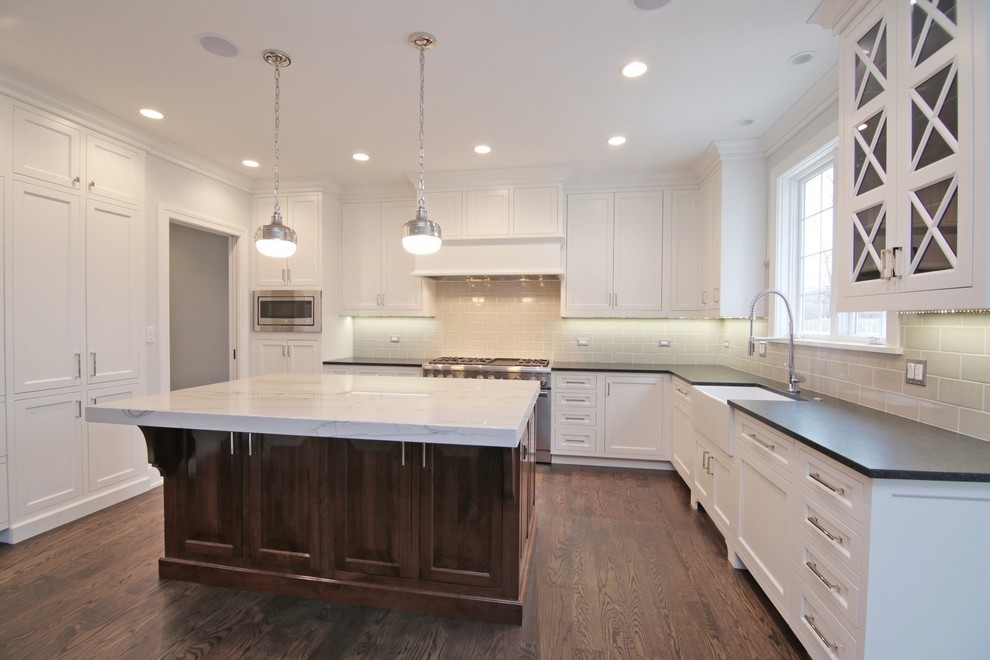 Example of a large transitional u-shaped dark wood floor and brown floor kitchen design in Chicago with a farmhouse sink, white cabinets, stainless steel appliances, an island, gray backsplash, subway tile backsplash, shaker cabinets, solid surface countertops and black countertops