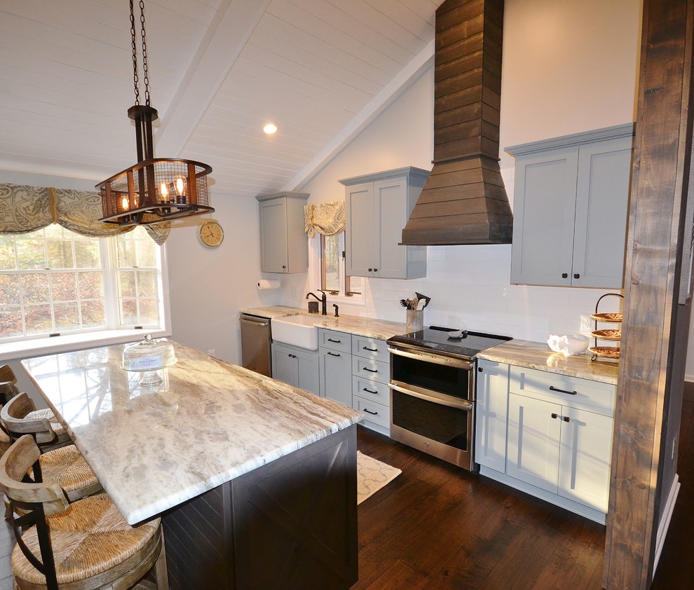 This is an example of a large country l-shaped eat-in kitchen in Philadelphia with a farmhouse sink, flat-panel cabinets, blue cabinets, granite benchtops, beige splashback, mosaic tile splashback, stainless steel appliances, dark hardwood floors, with island, brown floor and beige benchtop.