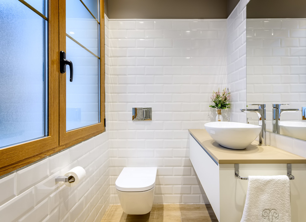 Inspiration for a mid-sized contemporary bathroom in Other with flat-panel cabinets, white cabinets, a wall-mount toilet, light hardwood floors, a vessel sink, beige benchtops, white tile, subway tile and brown walls.