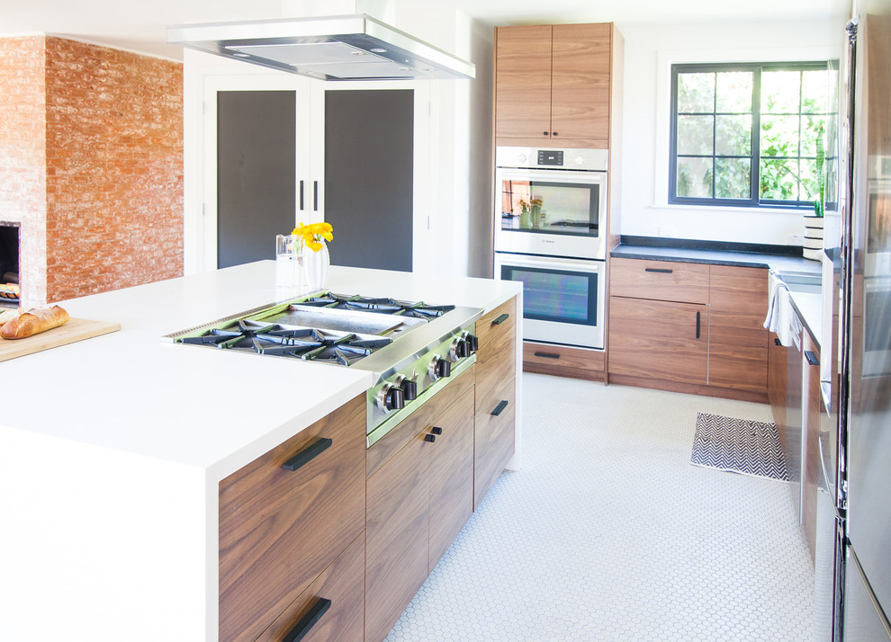 Photo of a small midcentury l-shaped open plan kitchen in San Francisco with flat-panel cabinets, medium wood cabinets, multi-coloured splashback, ceramic splashback, stainless steel appliances, porcelain floors, with island, white floor, a farmhouse sink and soapstone benchtops.