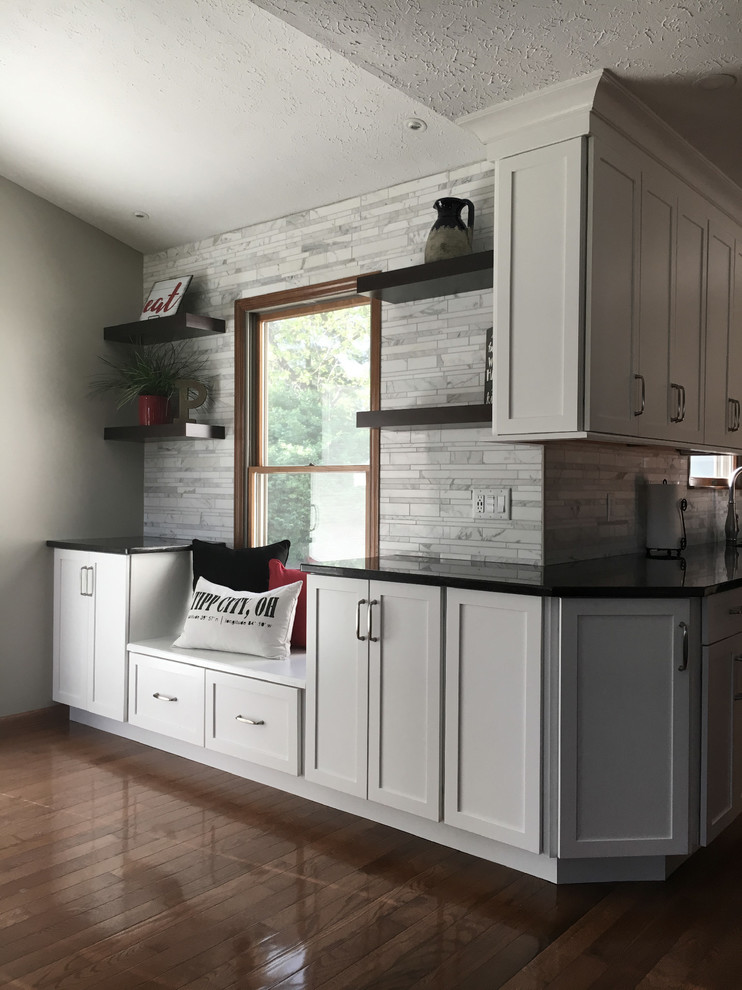 Large transitional single-wall medium tone wood floor eat-in kitchen photo with an undermount sink, shaker cabinets, white cabinets, granite countertops, multicolored backsplash, marble backsplash, stainless steel appliances, an island and black countertops