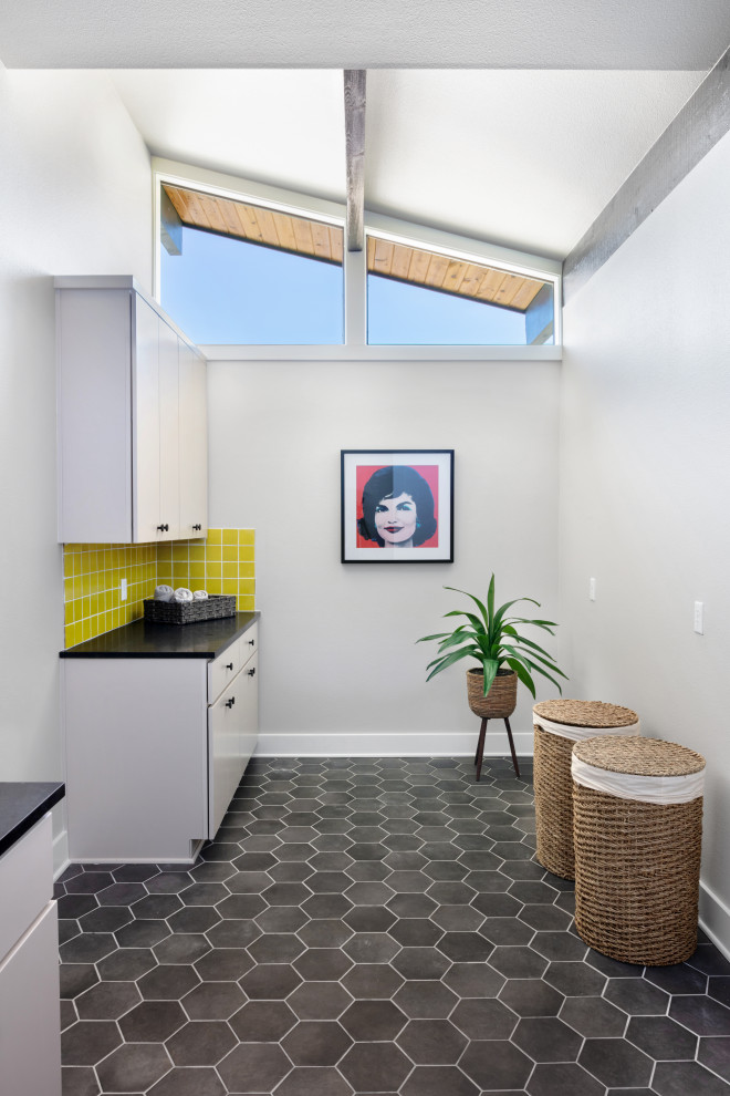Photo of a mid-sized midcentury single-wall dedicated laundry room in Austin with flat-panel cabinets, white cabinets, quartzite benchtops, yellow splashback, subway tile splashback, white walls, porcelain floors, a side-by-side washer and dryer, black floor and black benchtop.
