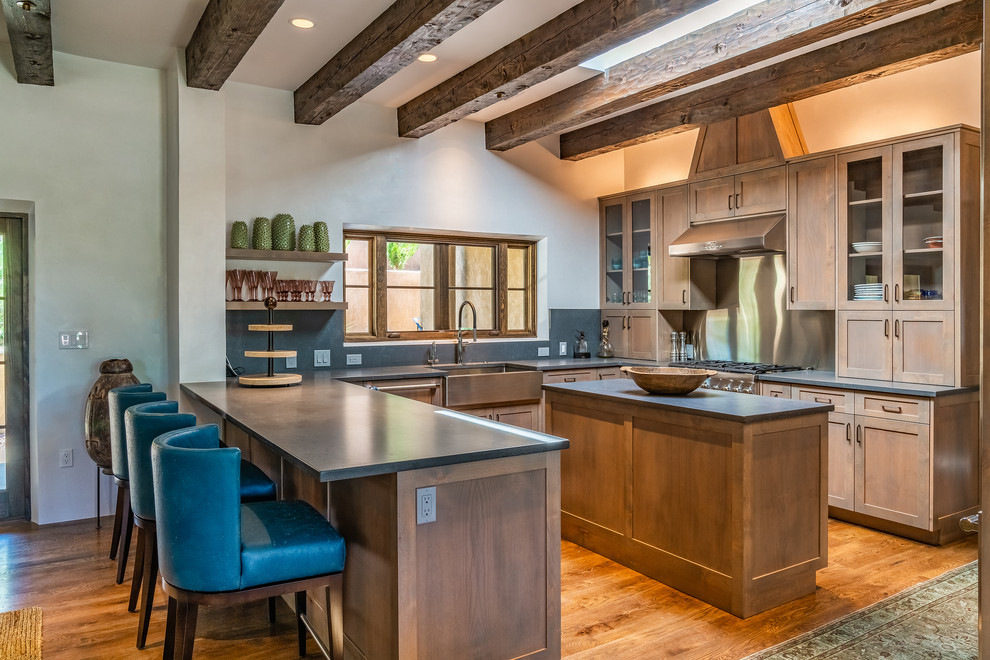 Photo of a mediterranean u-shaped kitchen in Albuquerque with a farmhouse sink, shaker cabinets, light wood cabinets, metallic splashback, panelled appliances, medium hardwood floors, with island and grey benchtop.