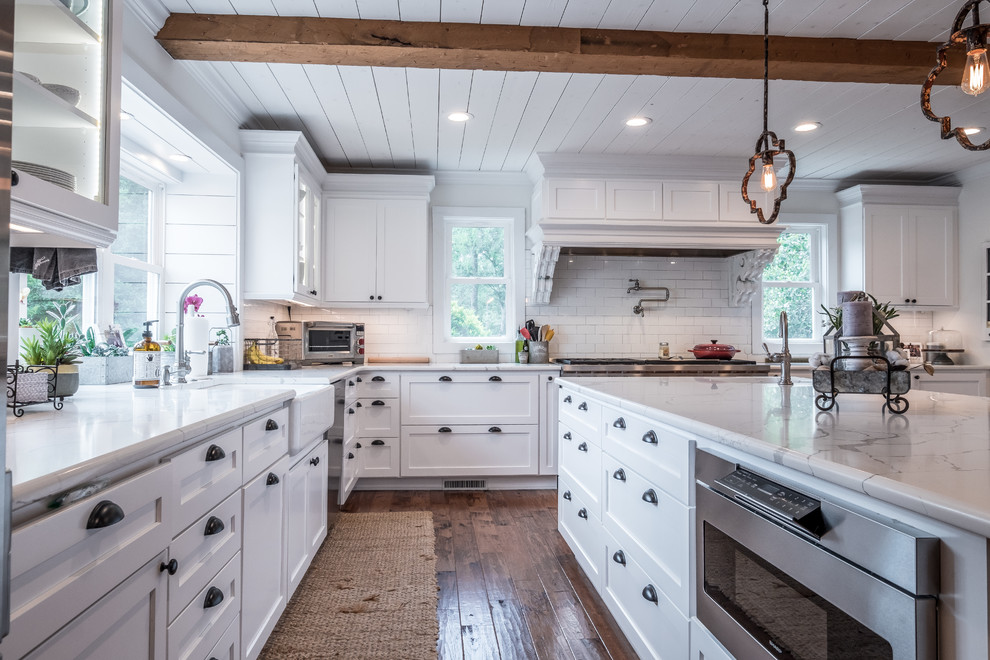 This is an example of an expansive country eat-in kitchen in Charlotte with a farmhouse sink, white cabinets, quartz benchtops, white splashback, subway tile splashback, stainless steel appliances, with island, brown floor, white benchtop, shaker cabinets and dark hardwood floors.