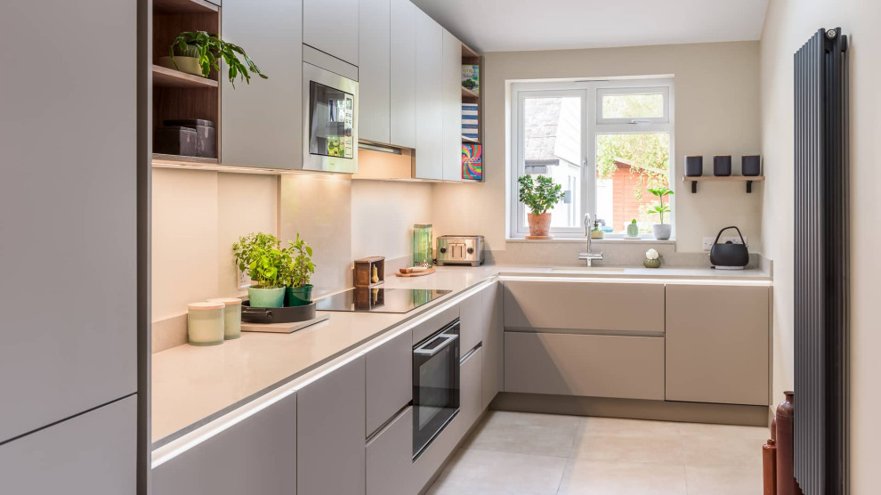 This is an example of a mid-sized contemporary l-shaped separate kitchen in Sussex with flat-panel cabinets and black appliances.