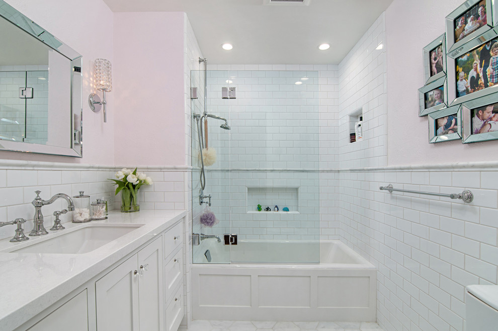 This is an example of a mid-sized traditional kids bathroom in San Diego with raised-panel cabinets, white cabinets, a drop-in tub, a shower/bathtub combo, white tile, ceramic tile, pink walls and porcelain floors.