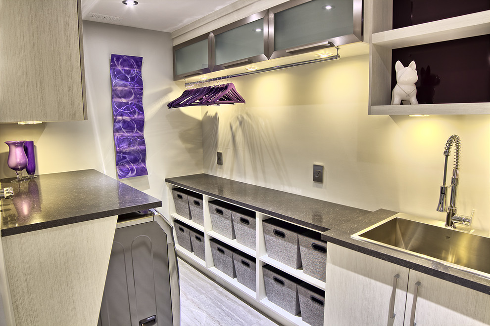 Inspiration for a mid-sized contemporary galley dedicated laundry room in Other with glass-front cabinets, beige cabinets, quartzite benchtops, beige walls, ceramic floors, a side-by-side washer and dryer and a drop-in sink.