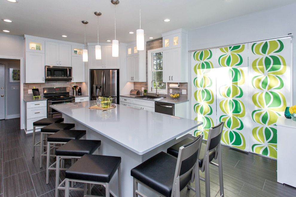 Example of a mid-sized transitional u-shaped porcelain tile enclosed kitchen design with a drop-in sink, recessed-panel cabinets, white cabinets, quartz countertops, gray backsplash, ceramic backsplash, stainless steel appliances and an island