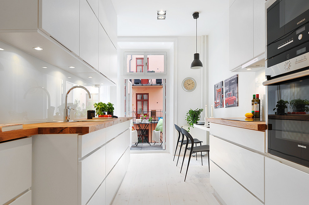 Photo of a mid-sized scandinavian galley eat-in kitchen in Stockholm with flat-panel cabinets, white cabinets, wood benchtops, white splashback, glass sheet splashback, painted wood floors, no island and a drop-in sink.