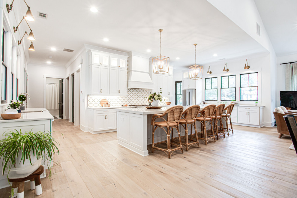 Design ideas for a large country u-shaped open plan kitchen in Atlanta with a farmhouse sink, shaker cabinets, white cabinets, quartz benchtops, white splashback, mosaic tile splashback, stainless steel appliances, light hardwood floors, with island, beige floor, grey benchtop and vaulted.