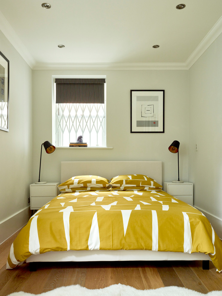 Mid-sized contemporary bedroom in London with white walls, light hardwood floors and beige floor.