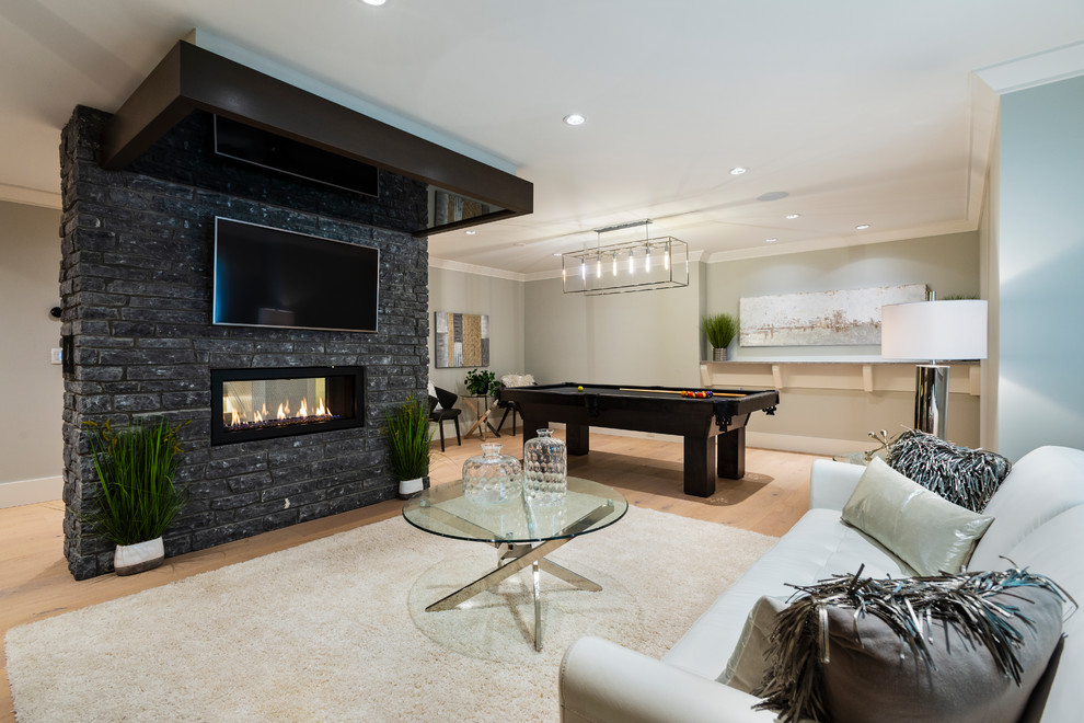 Photo of a mid-sized transitional fully buried basement in Vancouver with grey walls, light hardwood floors, a two-sided fireplace, a stone fireplace surround and beige floor.