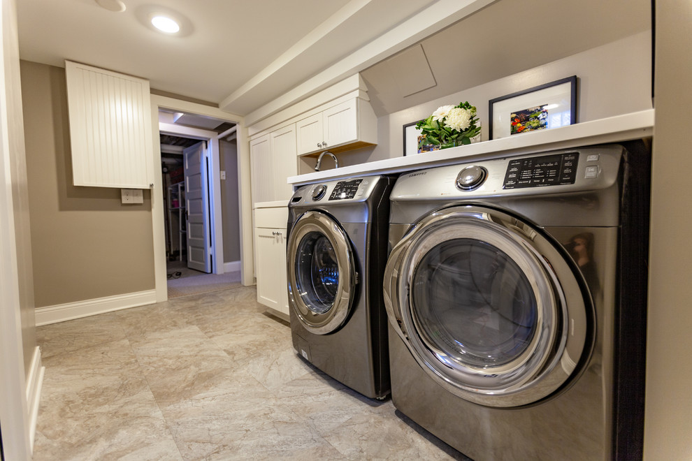 Inspiration for a large traditional single-wall dedicated laundry room in Minneapolis with an undermount sink, beaded inset cabinets, white cabinets, marble benchtops, beige walls, vinyl floors, a side-by-side washer and dryer, beige floor and white benchtop.