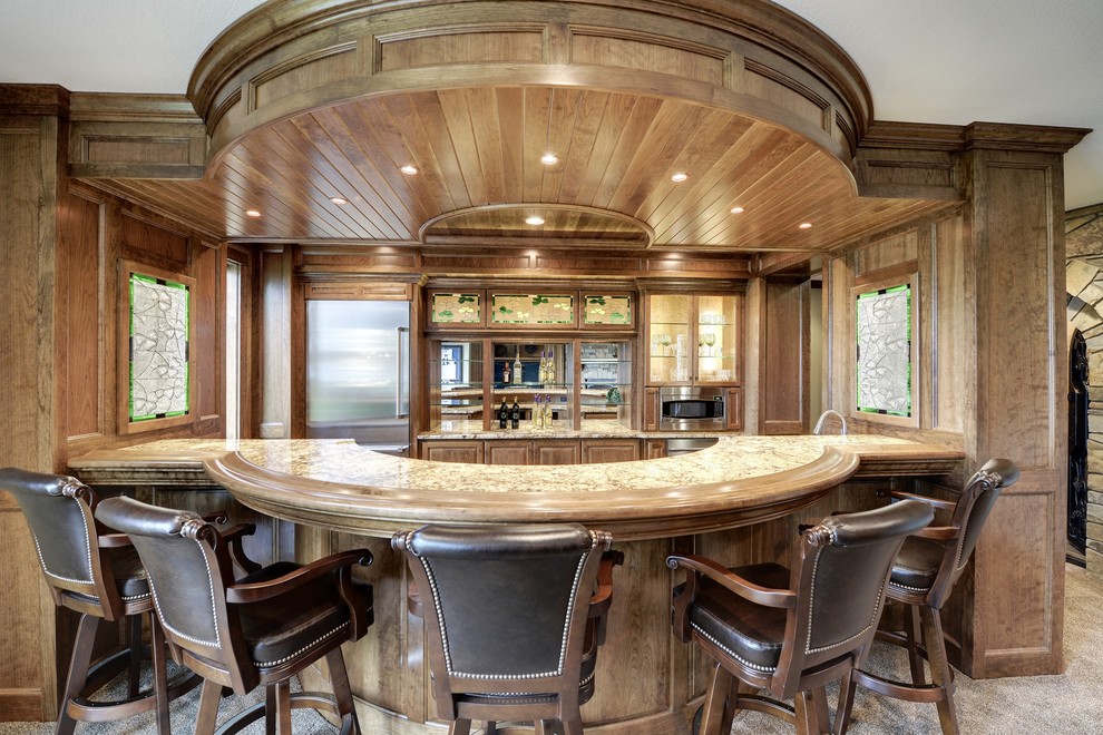 Photo of a large traditional galley seated home bar in Minneapolis with raised-panel cabinets, medium wood cabinets, mirror splashback and carpet.