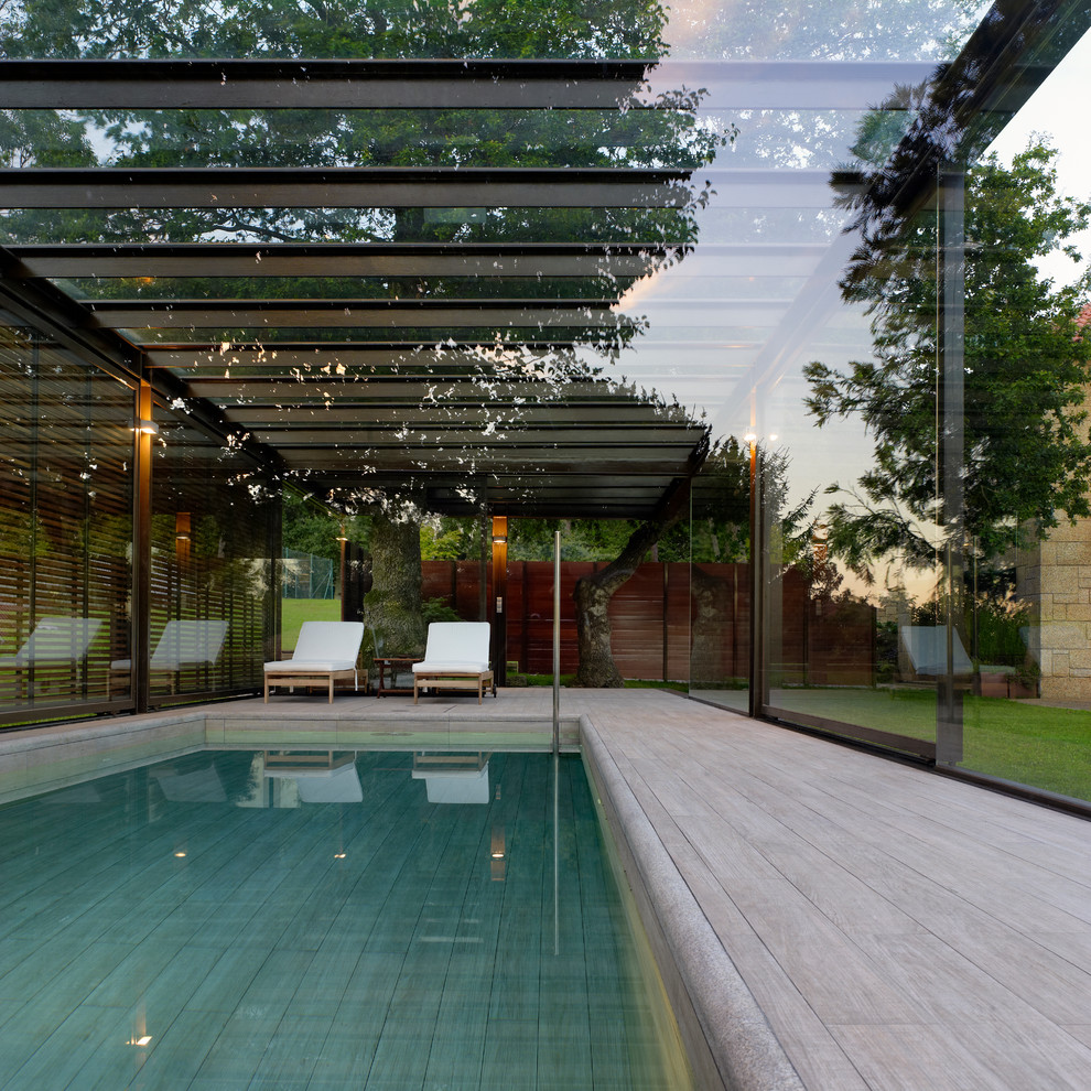 This is an example of a large contemporary indoor rectangular pool in Other with a pool house and decking.