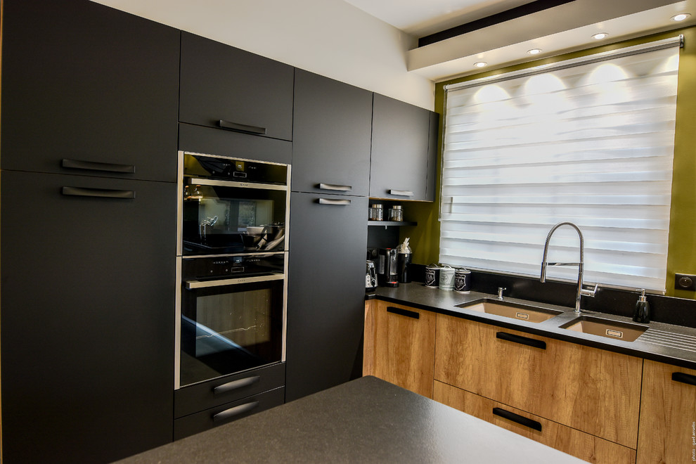 Photo of an expansive modern single-wall open plan kitchen in Lille with a double-bowl sink, light wood cabinets, granite benchtops, green splashback, stainless steel appliances, with island and black benchtop.