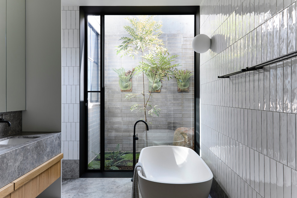 Mid-sized modern master bathroom in Melbourne with furniture-like cabinets, medium wood cabinets, a freestanding tub, white tile, subway tile, ceramic floors, an undermount sink, granite benchtops, grey floor and grey benchtops.