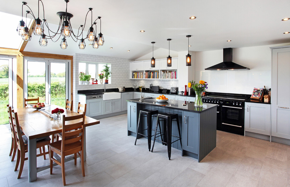 Design ideas for a large transitional u-shaped eat-in kitchen in Manchester with a farmhouse sink, shaker cabinets, white splashback, subway tile splashback, black appliances and with island.