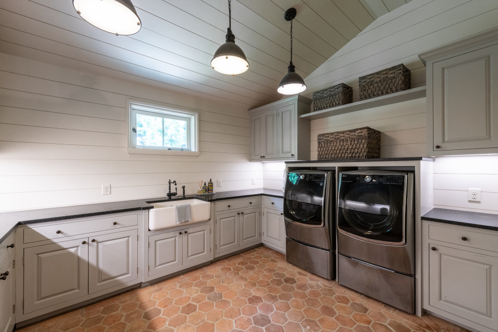 Large elegant u-shaped terra-cotta tile, orange floor, shiplap ceiling and shiplap wall dedicated laundry room photo in Atlanta with a farmhouse sink, raised-panel cabinets, gray cabinets, solid surface countertops, shiplap backsplash, beige walls, a side-by-side washer/dryer and black countertops