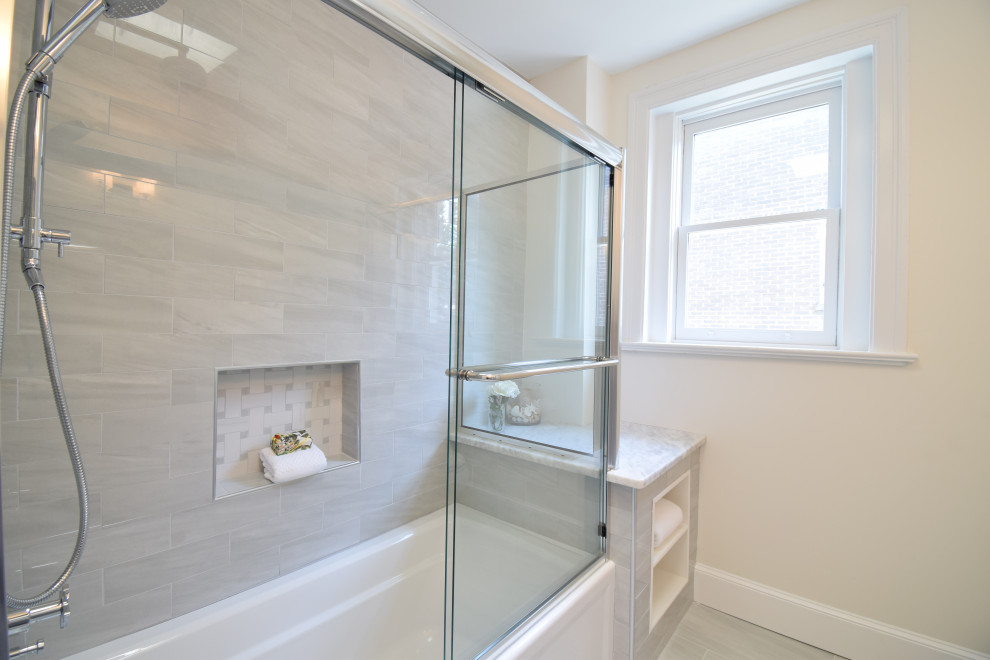 Photo of a mid-sized transitional kids bathroom in DC Metro with recessed-panel cabinets, grey cabinets, an alcove tub, a two-piece toilet, gray tile, ceramic tile, white walls, ceramic floors, an undermount sink, marble benchtops, grey floor, a sliding shower screen and multi-coloured benchtops.