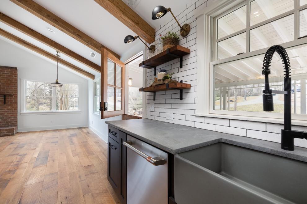 This is an example of a small country u-shaped eat-in kitchen with a farmhouse sink, shaker cabinets, black cabinets, concrete benchtops, white splashback, ceramic splashback, stainless steel appliances, medium hardwood floors, no island, brown floor and grey benchtop.