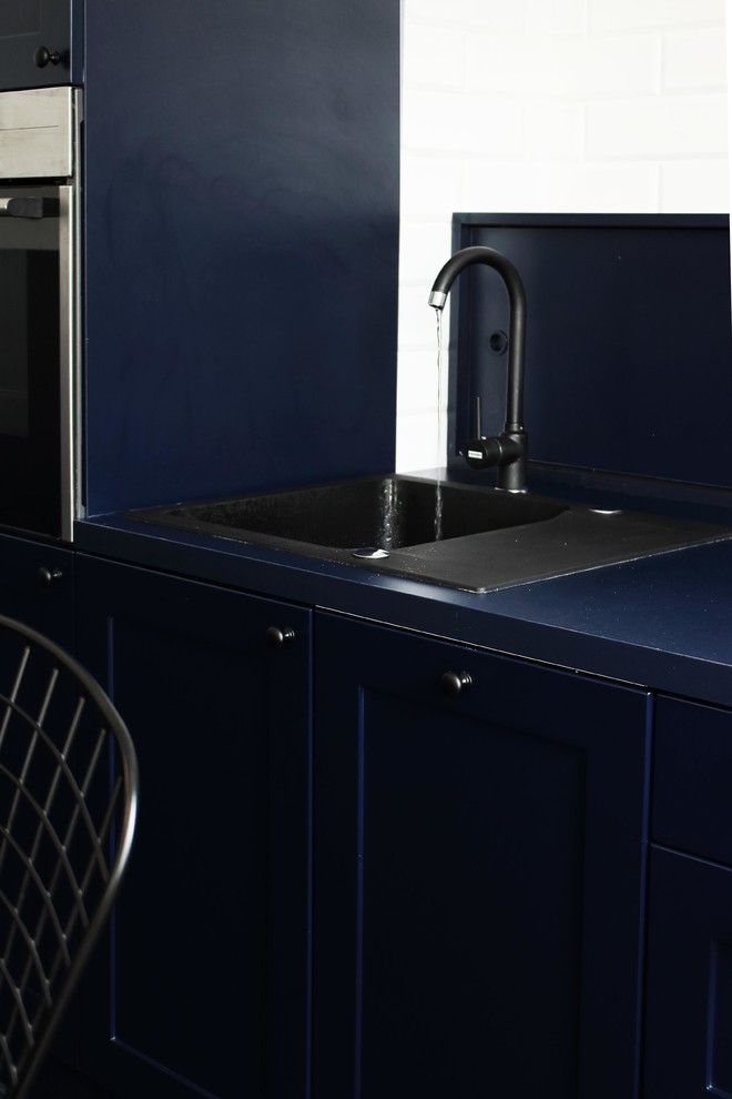 This is an example of a mid-sized industrial galley open plan kitchen in London with a single-bowl sink, beaded inset cabinets, blue cabinets, laminate benchtops, blue splashback, brick splashback, black appliances, porcelain floors, with island, blue floor and blue benchtop.
