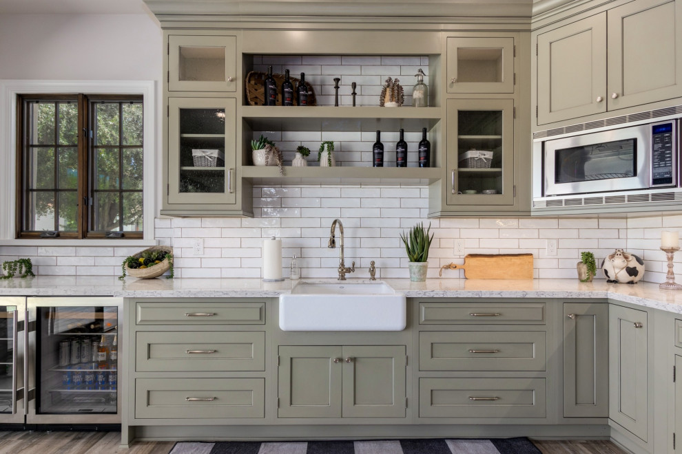 Photo of a country l-shaped kitchen in Phoenix with a farmhouse sink, green cabinets, white splashback, stainless steel appliances, recessed-panel cabinets, subway tile splashback, dark hardwood floors, brown floor and grey benchtop.