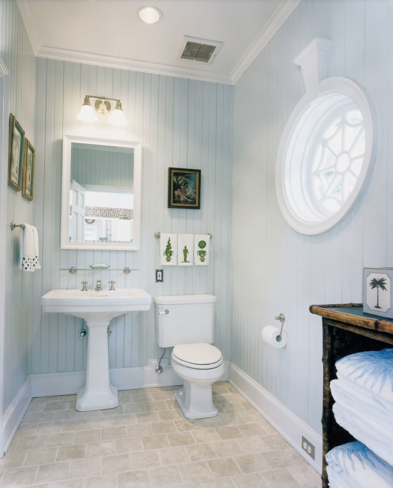 This is an example of a traditional powder room in New York with a pedestal sink, blue walls and travertine floors.