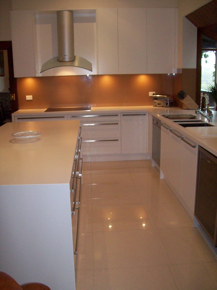 Large modern u-shaped eat-in kitchen in Sydney with an undermount sink, white cabinets, solid surface benchtops, orange splashback, glass sheet splashback, stainless steel appliances, porcelain floors and with island.