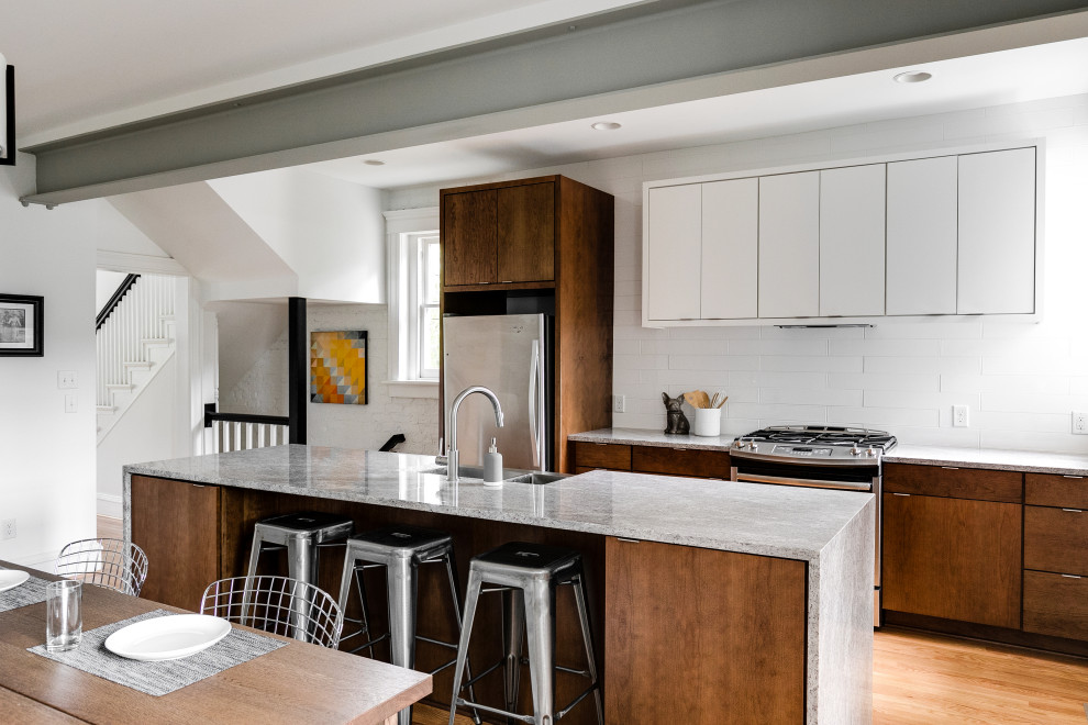 This is an example of a mid-sized transitional single-wall eat-in kitchen in Richmond with an undermount sink, flat-panel cabinets, medium wood cabinets, granite benchtops, white splashback, ceramic splashback, stainless steel appliances, light hardwood floors, with island and grey benchtop.