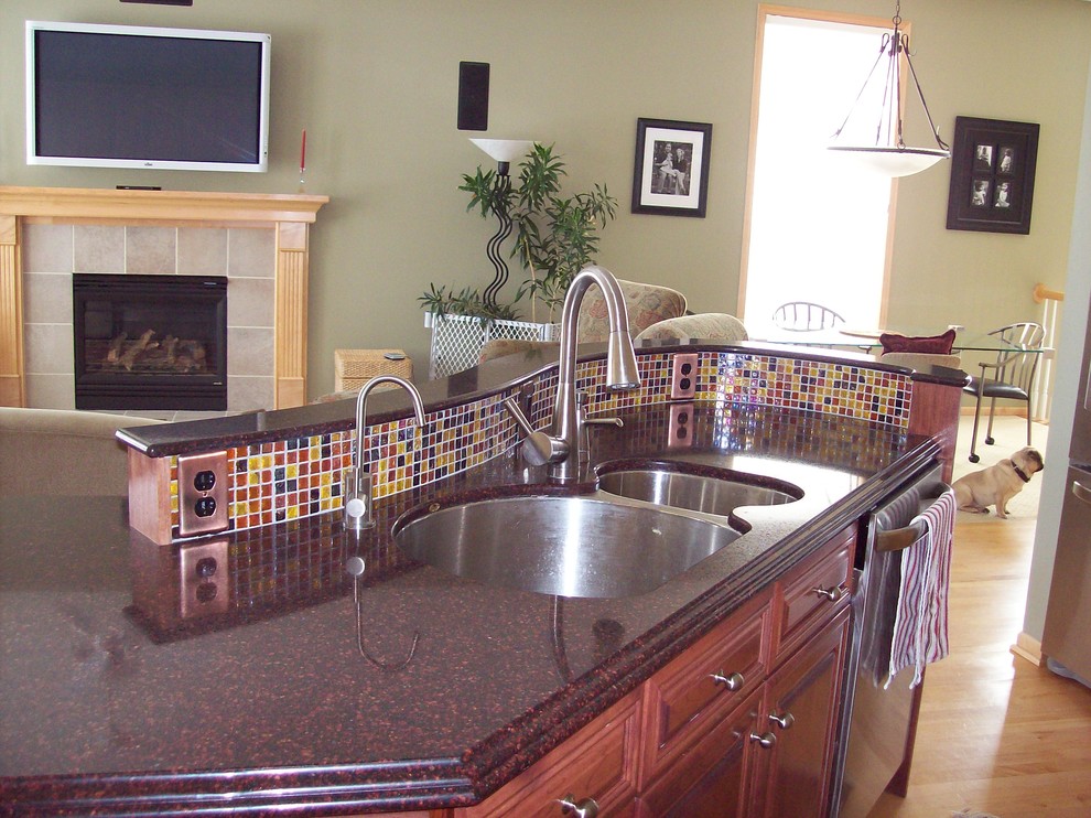 Photo of a large contemporary l-shaped open plan kitchen in Minneapolis with an undermount sink, raised-panel cabinets, light wood cabinets, granite benchtops, multi-coloured splashback, glass tile splashback, stainless steel appliances, light hardwood floors and with island.